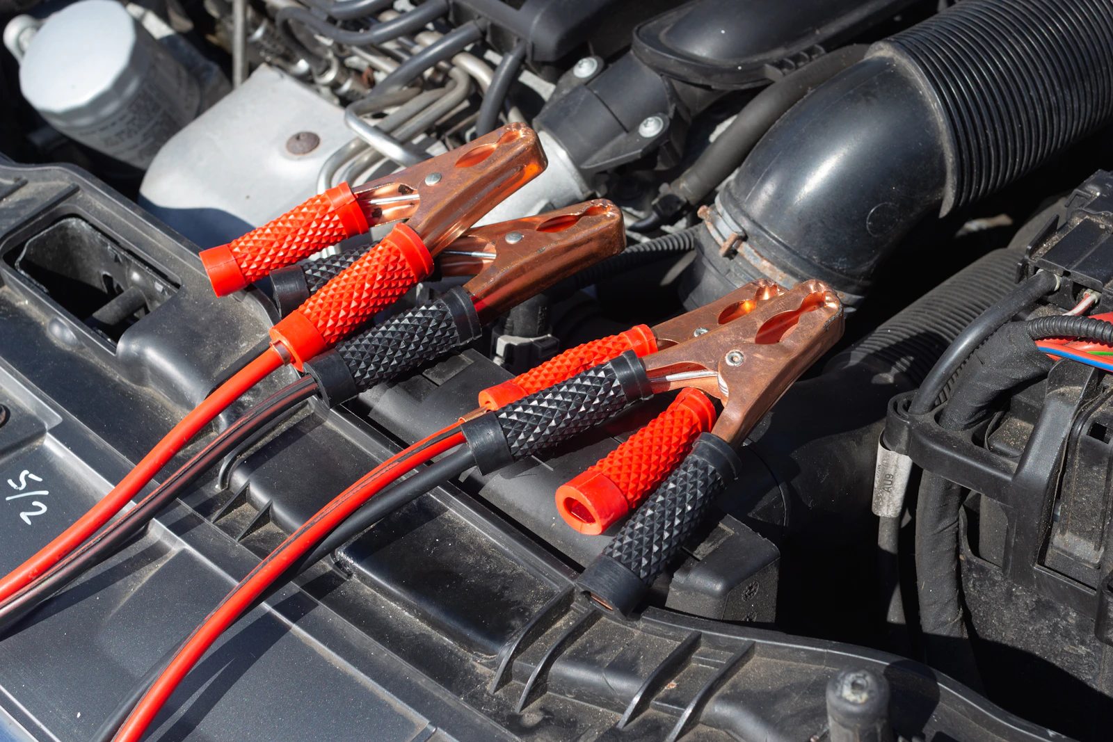 Rote und schwarze Starthilfeklemmen im Motorraum eines Fahrzeugs